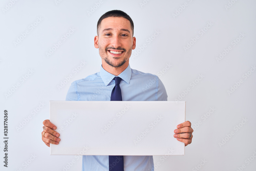 Young business man holding blank banner over isolated background with a happy face standing and smiling with a confident smile showing teeth Young business man holding blank banner over isolated background with a happy face standing and smiling with a confident smile showing teeth