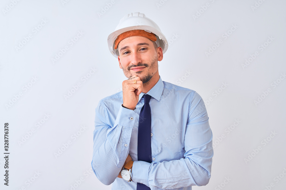 Young business man wearing contractor safety helmet over isolated background looking confident at the camera smiling with crossed arms and hand raised on chin. Thinking positive.