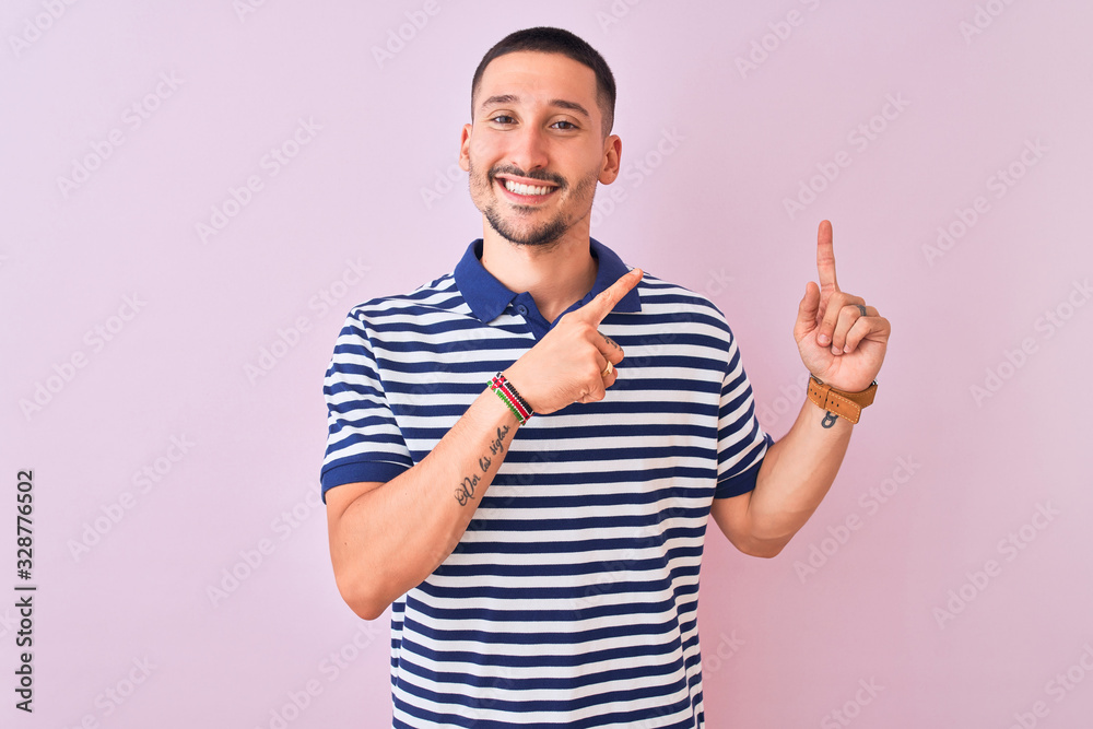 Young handsome man wearing nautical striped t-shirt over pink isolated background smiling and looking at the camera pointing with two hands and fingers to the side. Young handsome man wearing nautical striped t-shirt over pink isolated background smiling and looking at the camera pointing with two hands and fingers to the side.
