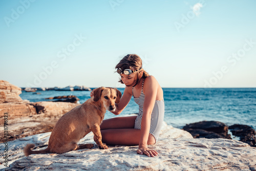 Girl embracing her dog while sitting on the rocky beach