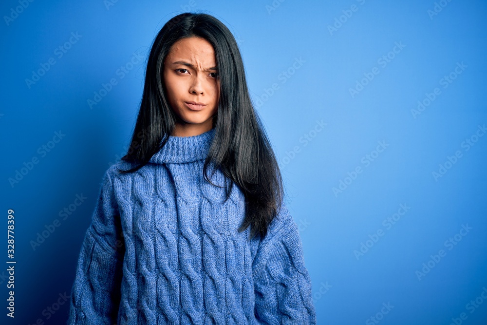 Young beautiful chinese woman wearing casual sweater over isolated blue background skeptic and nervous, frowning upset because of problem. Negative person. Young beautiful chinese woman wearing casual sweater over isolated blue background skeptic and nervous, frowning upset because of problem. Negative person.