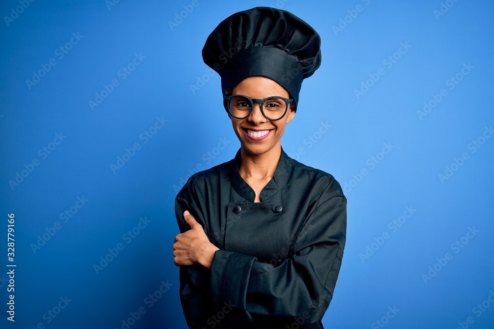 Young african american chef woman wearing cooker uniform and hat over blue background happy face smiling with crossed arms looking at the camera. Positive person. Young african american chef woman wearing cooker uniform and hat over blue background happy face smiling with crossed arms looking at the camera. Positive person.