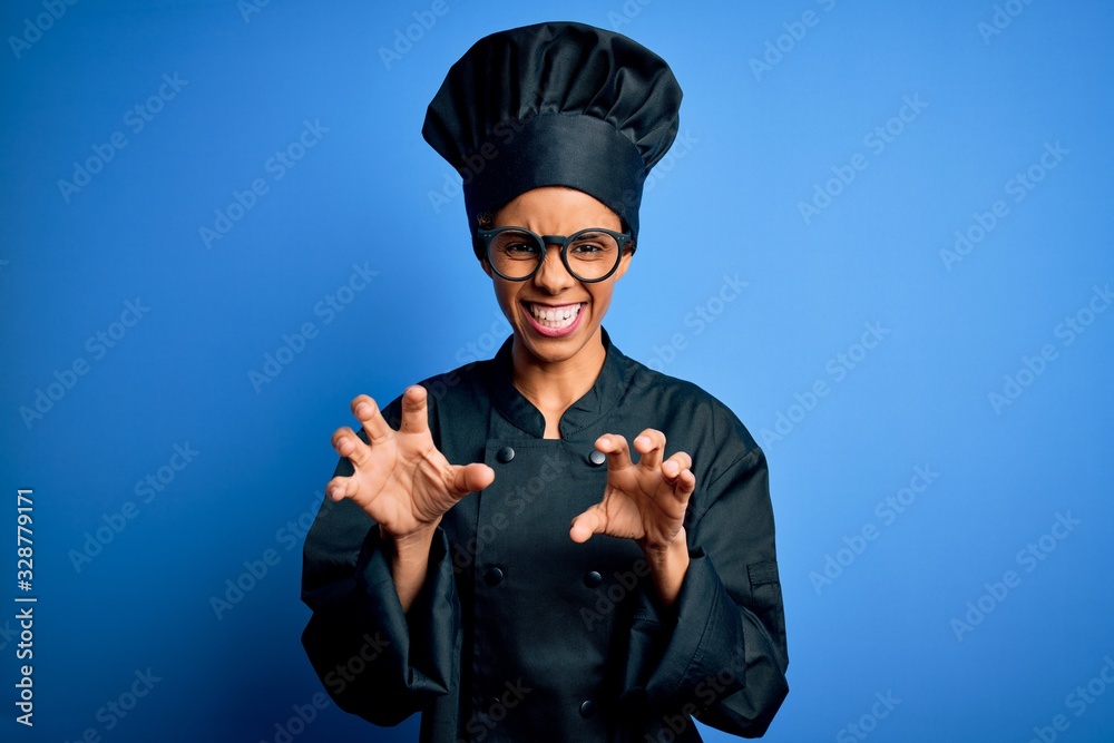 Young african american chef woman wearing cooker uniform and hat over blue background smiling funny doing claw gesture as cat, aggressive and sexy expression Young african american chef woman wearing cooker uniform and hat over blue background smiling funny doing claw gesture as cat, aggressive and sexy expression