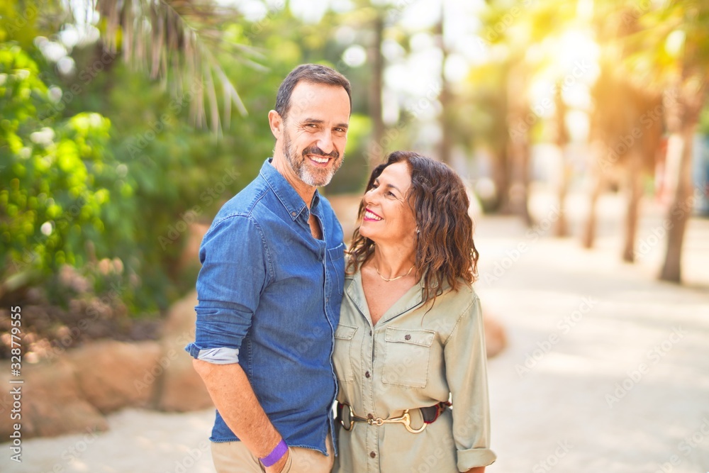 Fototapeta premium Middle age beautiful couple smiling happy and confident at town park. Standing with smile on face and hugging
