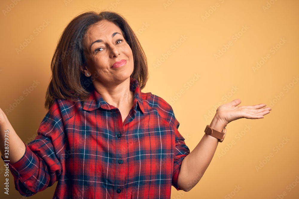 Middle age beautiful woman wearing casual shirt standing over isolated yellow background clueless and confused expression with arms and hands raised. Doubt concept. Middle age beautiful woman wearing casual shirt standing over isolated yellow background clueless and confused expression with arms and hands raised. Doubt concept.