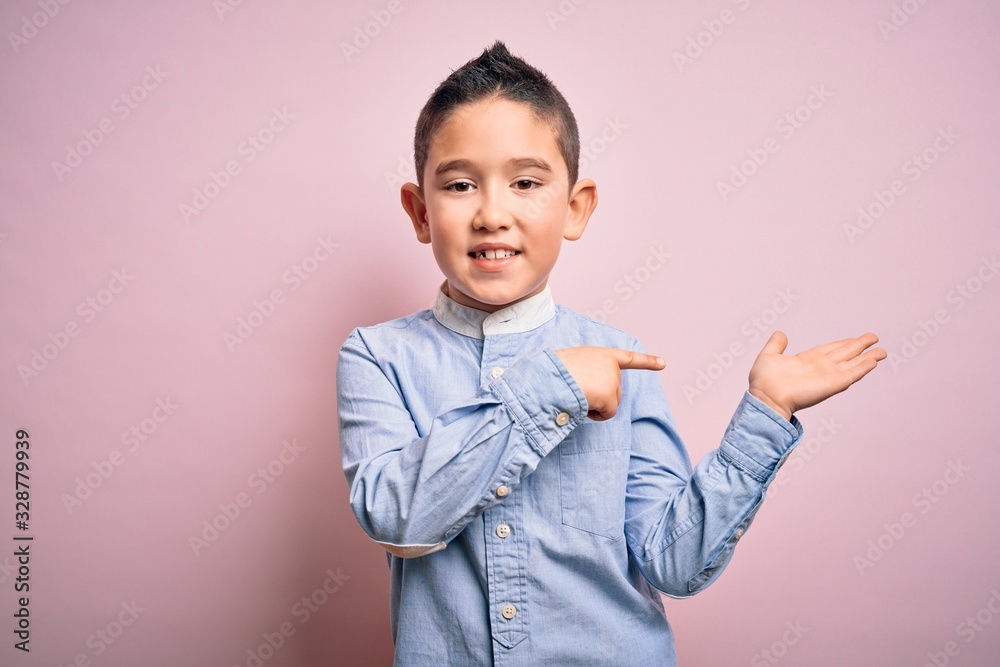 Young little boy kid wearing elegant shirt standing over pink isolated background amazed and smiling to the camera while presenting with hand and pointing with finger. Young little boy kid wearing elegant shirt standing over pink isolated background amazed and smiling to the camera while presenting with hand and pointing with finger.