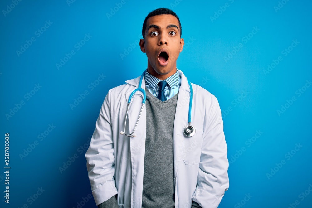 Handsome african american doctor man wearing coat and stethoscope over blue background afraid and shocked with surprise and amazed expression, fear and excited face. Handsome african american doctor man wearing coat and stethoscope over blue background afraid and shocked with surprise and amazed expression, fear and excited face.