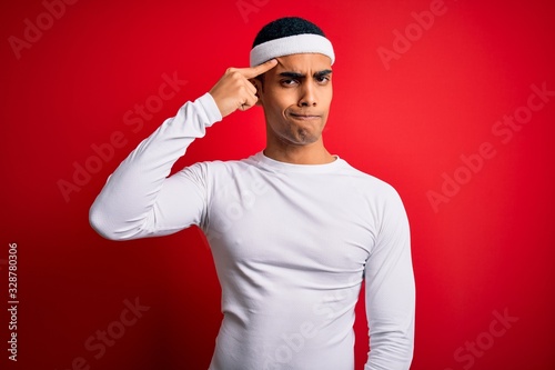 Young handsome african american sportsman wearing sportswear over red background pointing unhappy to pimple on forehead, ugly infection of blackhead. Acne and skin problem