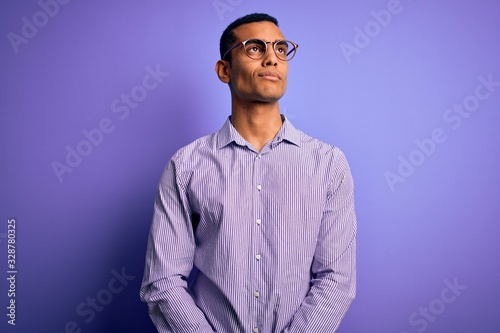 Handsome african american man wearing striped shirt and glasses over purple background smiling looking to the side and staring away thinking.