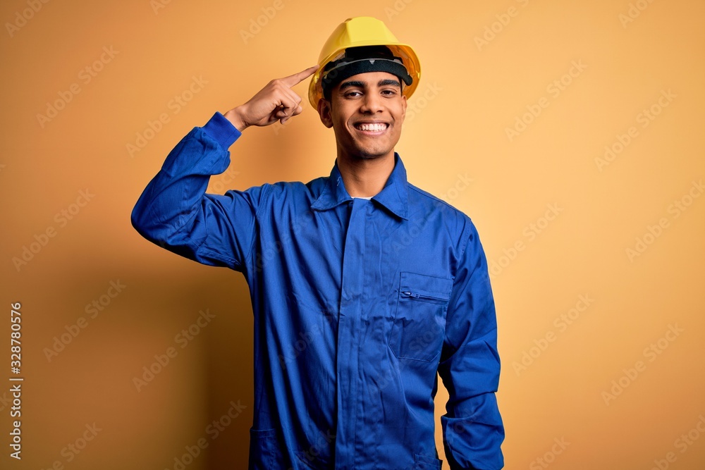 Young handsome african american worker man wearing blue uniform and security helmet Smiling pointing to head with one finger, great idea or thought, good memory Young handsome african american worker man wearing blue uniform and security helmet Smiling pointing to head with one finger, great idea or thought, good memory