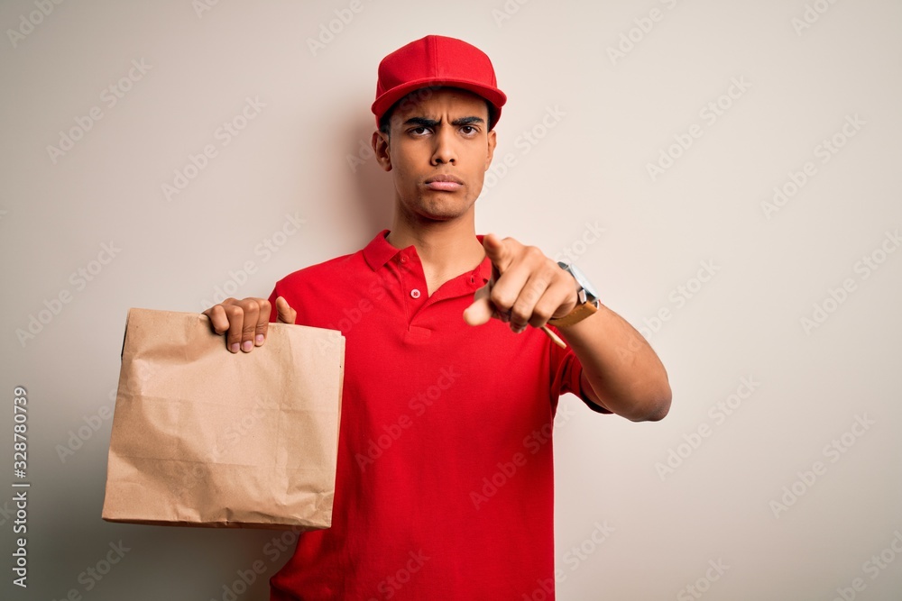 Young handsome african american delivery man holding paper bag with takeaway food pointing with finger to the camera and to you, hand sign, positive and confident gesture from the front