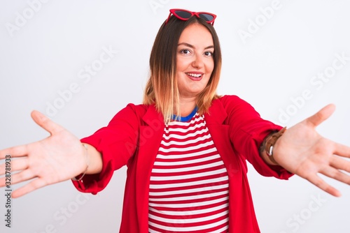 Young beautiful woman wearing striped t-shirt and jacket over isolated white background looking at the camera smiling with open arms for hug. Cheerful expression embracing happiness.