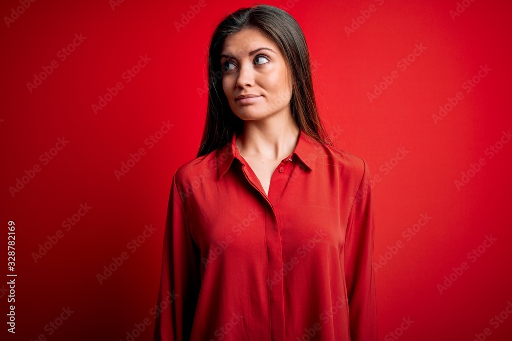 Young beautiful woman with blue eyes wearing casual shirt standing over red background smiling looking to the side and staring away thinking. Young beautiful woman with blue eyes wearing casual shirt standing over red background smiling looking to the side and staring away thinking.