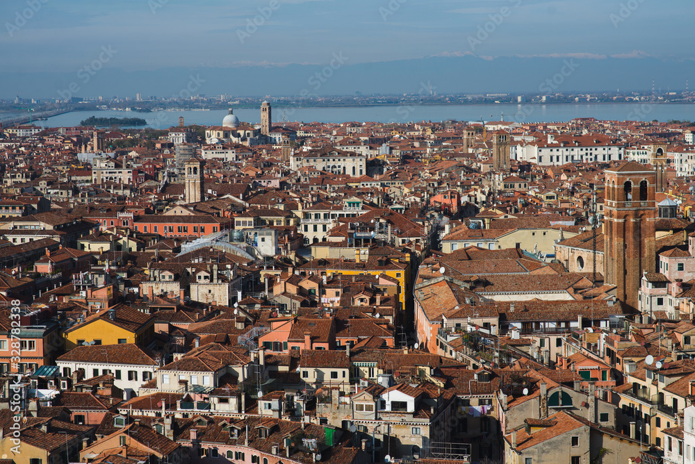 Top view of traditional buildings in the center of Venice. Skyline in the city, view of the red roofs from the tower. Warm autumn day while traveling in Europe. A romantic look. Blue sky with clouds.
