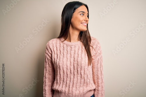 Young beautiful brunette woman wearing casual sweater over isolated white background looking away to side with smile on face, natural expression. Laughing confident.