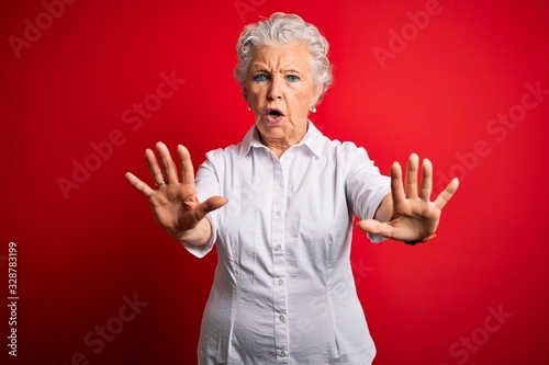 Senior beautiful woman wearing elegant shirt standing over isolated red background doing stop gesture with hands palms, angry and frustration expression