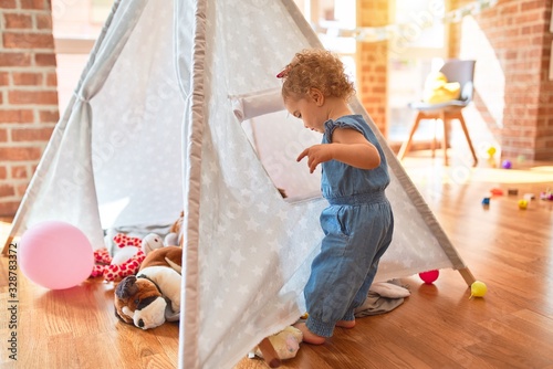 Beautiful caucasian infant playing with toys at colorful playroom. Happy and playful with indian tent at kindergarten.