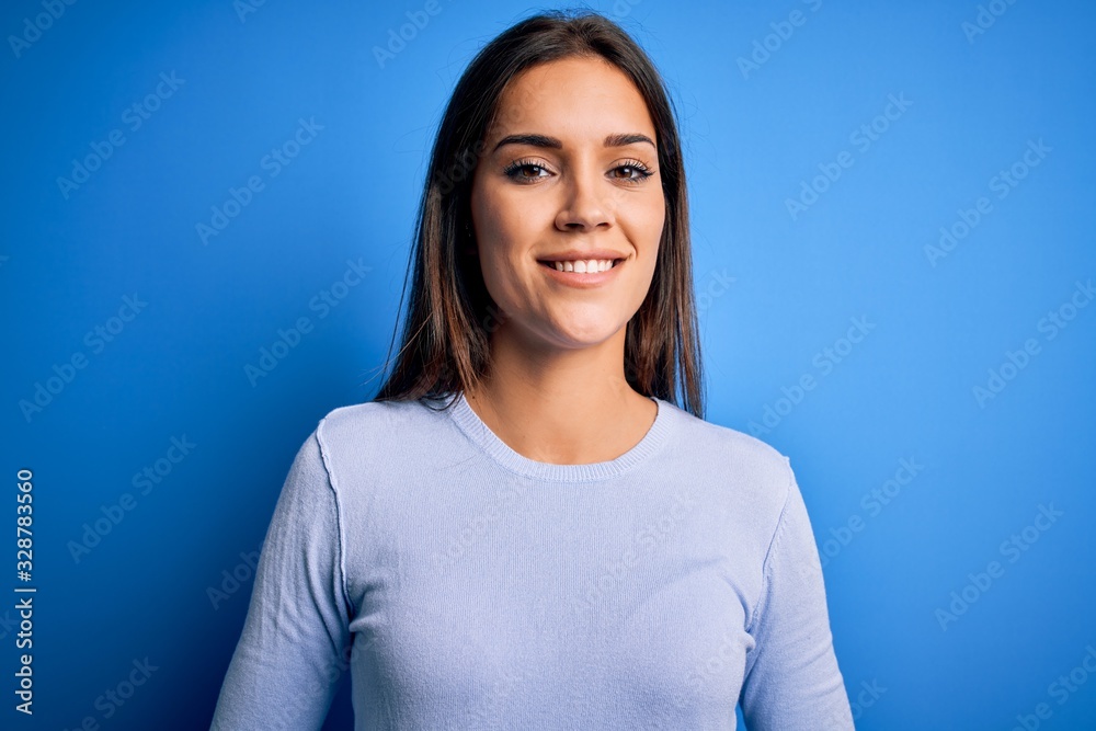 Obraz premium Young beautiful brunette woman wearing casual sweater standing over blue background with hands together and crossed fingers smiling relaxed and cheerful. Success and optimistic