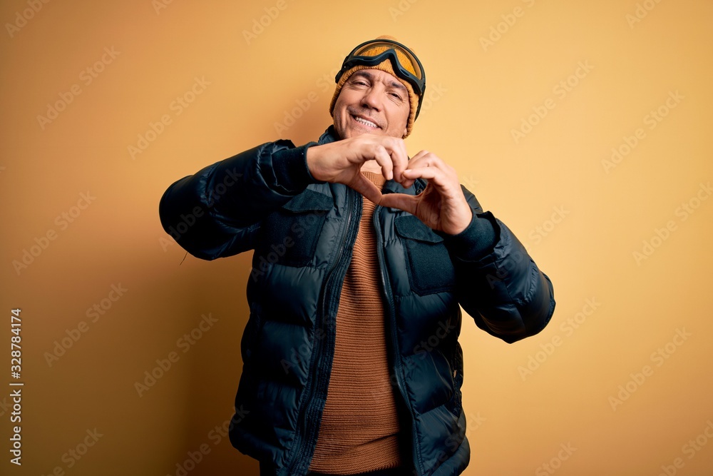 Middle age handsome grey-haired skier man on vacation wearing ski goggles smiling in love doing heart symbol shape with hands. Romantic concept. Middle age handsome grey-haired skier man on vacation wearing ski goggles smiling in love doing heart symbol shape with hands. Romantic concept.
