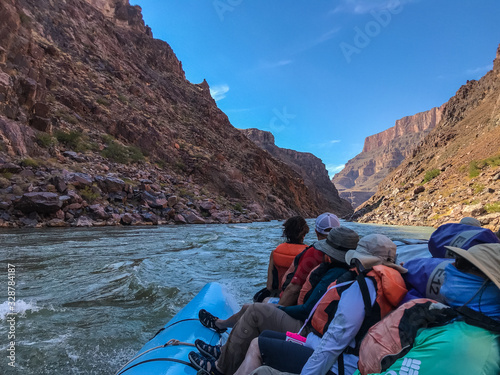 River trip group of people sitting on a blue s-rig raft and looking downstream on the Colorado River rapids in the Grand Canyon National Park, Arizona, United States of America