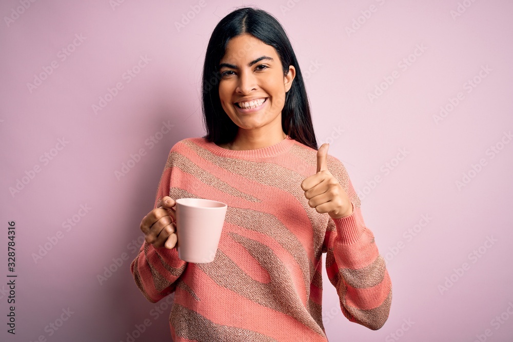 Young beautiful hispanic woman drinking a cup of hot coffee over pink isolated background happy with big smile doing ok sign, thumb up with fingers, excellent sign Young beautiful hispanic woman drinking a cup of hot coffee over pink isolated background happy with big smile doing ok sign, thumb up with fingers, excellent sign