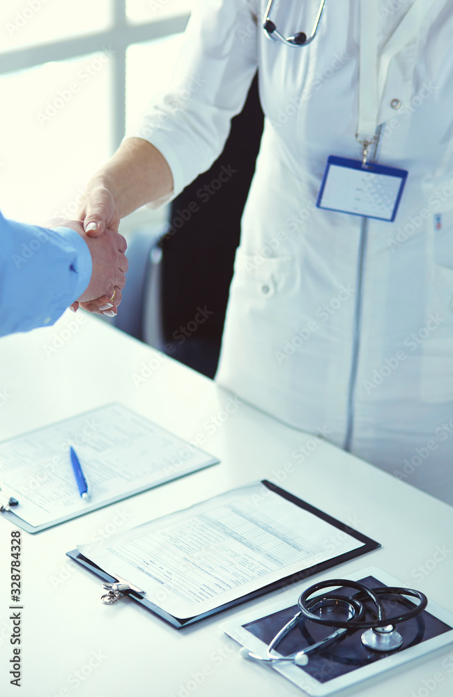 Female doctor handshaking a patient's hand and smiling Female doctor handshaking a patient's hand and smiling