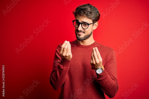 Fotografiet Young handsome man with beard wearing glasses and sweater standing over red back