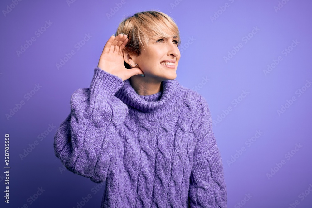 Young blonde woman with short hair wearing winter turtleneck sweater over purple background smiling with hand over ear listening an hearing to rumor or gossip. Deafness concept. Young blonde woman with short hair wearing winter turtleneck sweater over purple background smiling with hand over ear listening an hearing to rumor or gossip. Deafness concept.