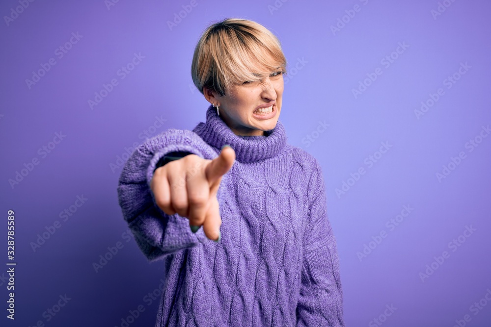 Young blonde woman with short hair wearing winter turtleneck sweater over purple background pointing displeased and frustrated to the camera, angry and furious with you Young blonde woman with short hair wearing winter turtleneck sweater over purple background pointing displeased and frustrated to the camera, angry and furious with you