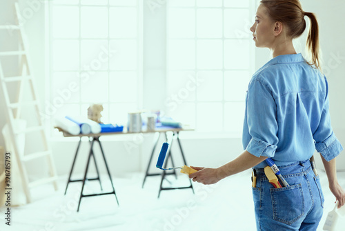 Pretty smilling woman painting interior wall of home with paint roller