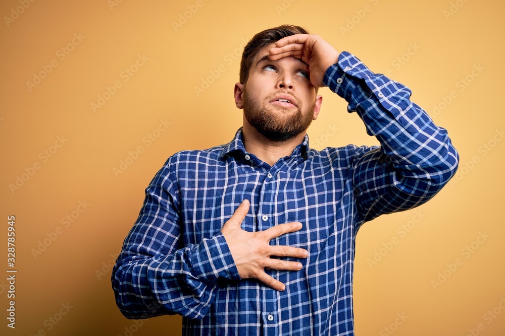 Young blond businessman with beard and blue eyes wearing shirt over yellow background Touching forehead for illness and fever, flu and cold, virus sick Young blond businessman with beard and blue eyes wearing shirt over yellow background Touching forehead for illness and fever, flu and cold, virus sick