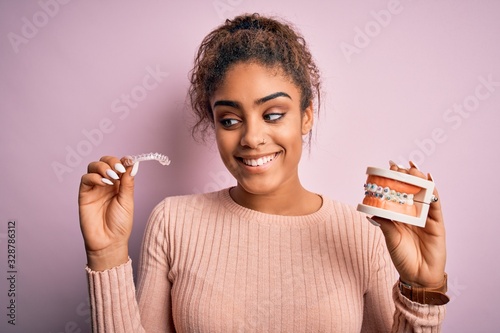 Young african american woman smiling happy holding professional orthodontic denture with metal braces and removable invisible aligner. Comparation of two dental straighten treatments photo