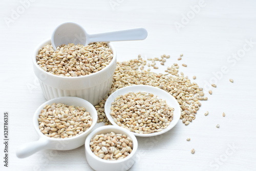 Raw barley grains, released in containers on white wooden background