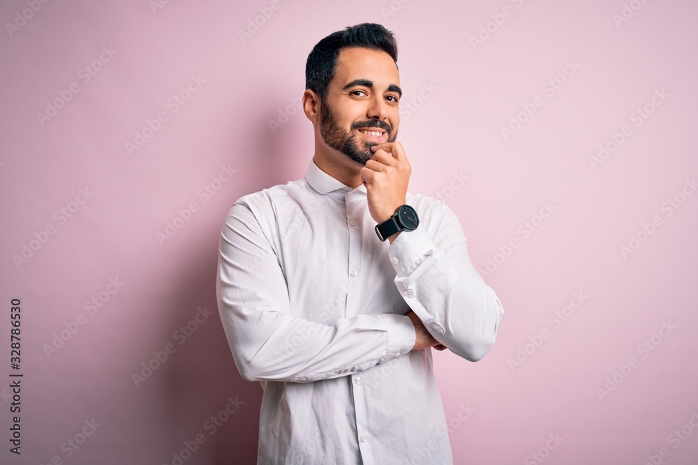 Young handsome man with beard wearing casual shirt standing over pink background looking confident at the camera with smile with crossed arms and hand raised on chin. Thinking positive. Young handsome man with beard wearing casual shirt standing over pink background looking confident at the camera with smile with crossed arms and hand raised on chin. Thinking positive.
