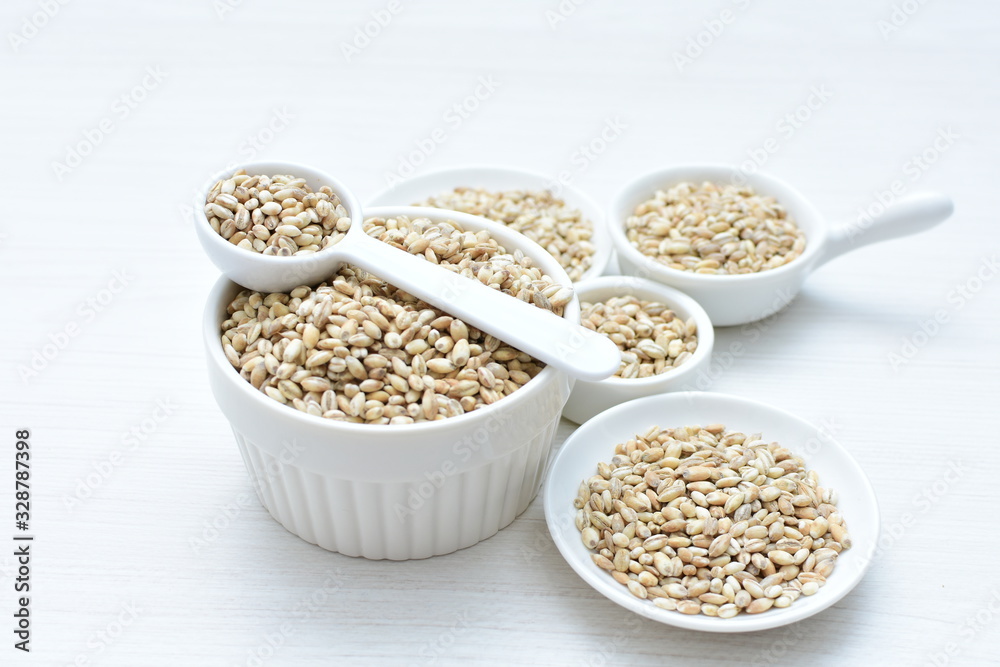 Raw barley grains, released in containers on white wooden background Raw barley grains, released in containers on white wooden background