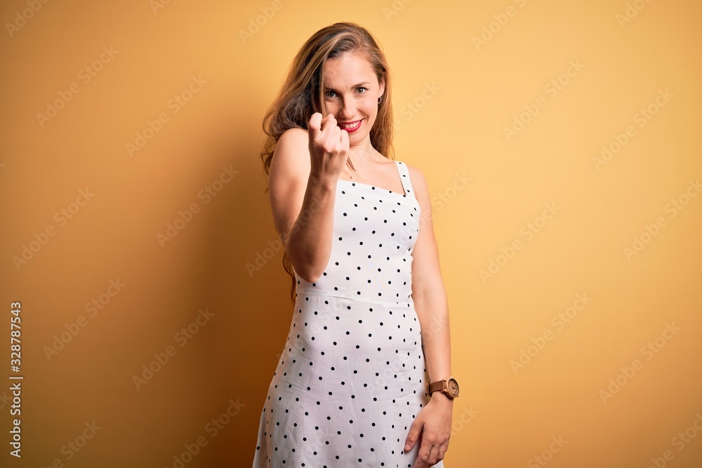 Young beautiful blonde woman on vacation wearing summer dress over yellow background Beckoning come here gesture with hand inviting welcoming happy and smiling Young beautiful blonde woman on vacation wearing summer dress over yellow background Beckoning come here gesture with hand inviting welcoming happy and smiling