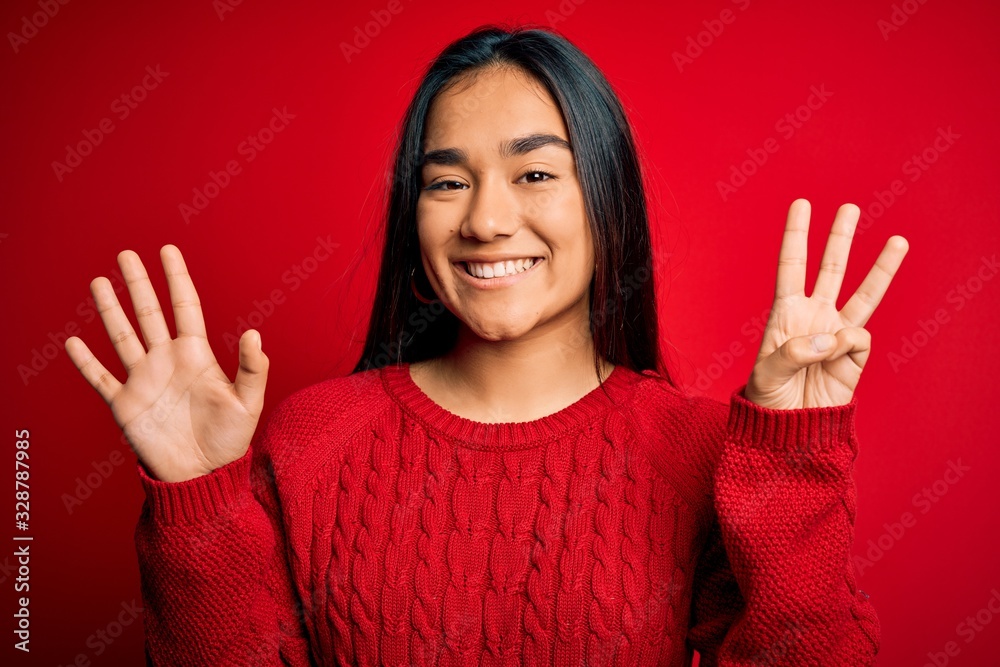 Young beautiful asian woman wearing casual sweater standing over isolated red background showing and pointing up with fingers number eight while smiling confident and happy.