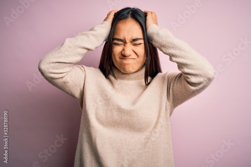 Young beautiful asian woman wearing casual turtleneck sweater over pink background suffering from headache desperate and stressed because pain and migraine. Hands on head. © Krakenimages.com