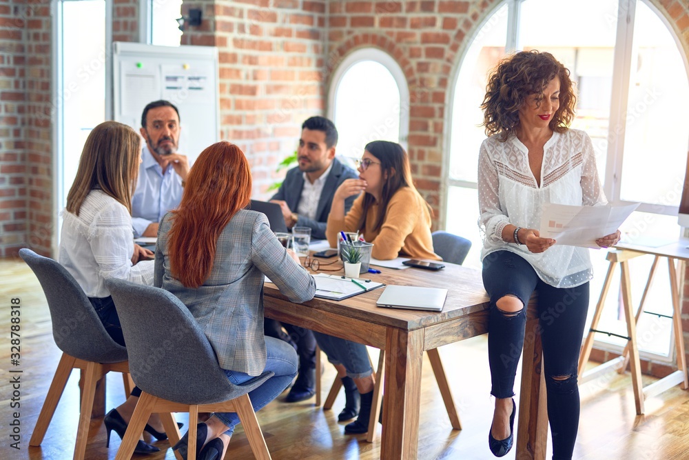 Group of business workers working together. Middle age beautiful businesswoman standing smiling happy looking at the camera at the office