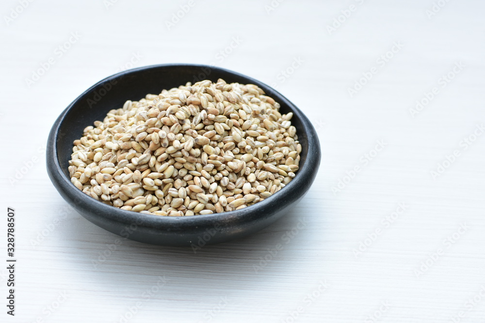 Raw barley grains, released in containers on white wooden background Raw barley grains, released in containers on white wooden background