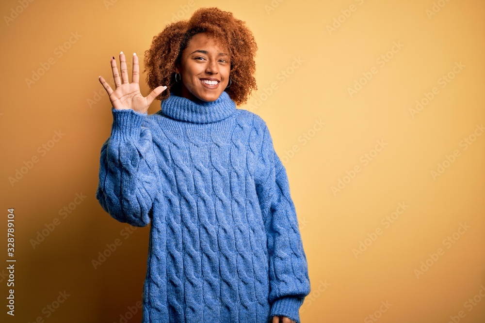 Young beautiful African American afro woman with curly hair wearing blue turtleneck sweater showing and pointing up with fingers number five while smiling confident and happy.