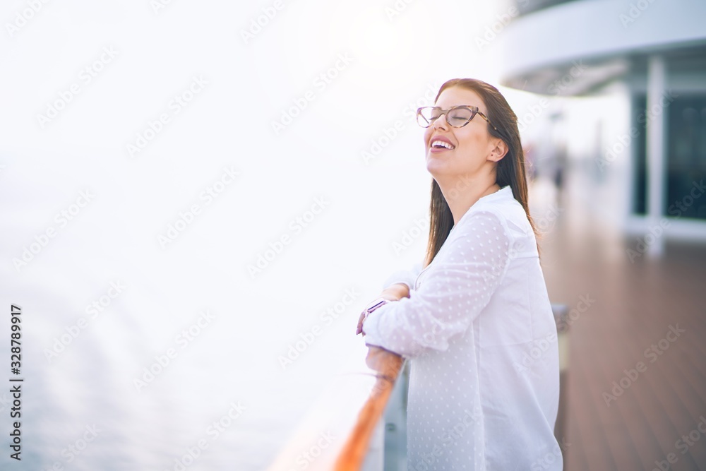 Young beautiful woman on vacation smiling happy and confident. Standing on a deck of ship with smile on face doing a cruise Young beautiful woman on vacation smiling happy and confident. Standing on a deck of ship with smile on face doing a cruise