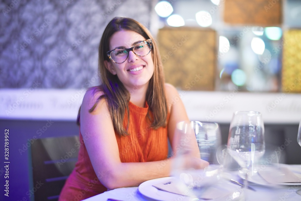 Young beautiful girl smiling happy and confident sitting on chair at restaurant. Relaxing with a smile on face Young beautiful girl smiling happy and confident sitting on chair at restaurant. Relaxing with a smile on face