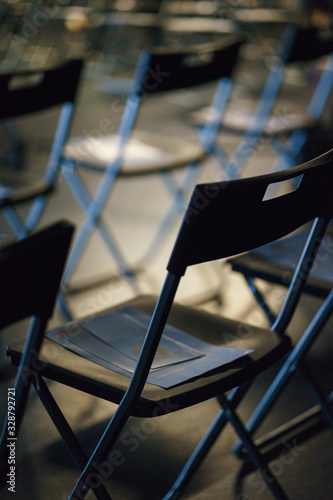 Rows of plastic black folding chairs in an empty auditorium prepared for guests and participants of the event. Presentation and training. Concept. Soft focus and bokeh.