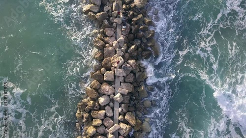 Aerial view of a Fishermen are standing on a breakwater and waves crashing on the breakwater.