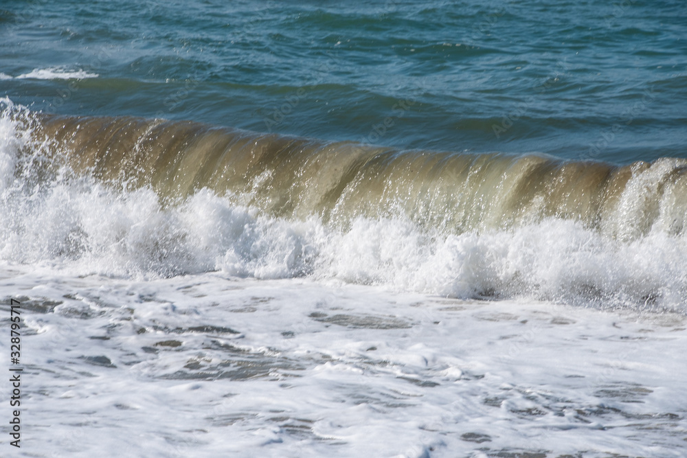 Fototapeta premium Mediterranean sea at sunset. Waves break on the sandy shore, sea foam. Natural background