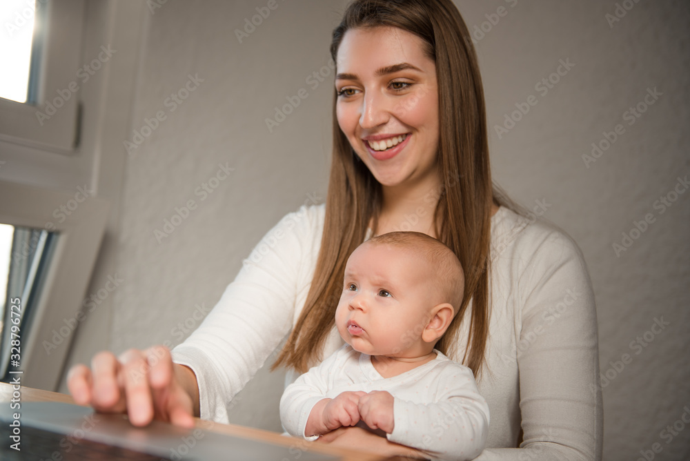 Young mother holds baby girl and works on laptop computer Young mother holds baby girl and works on laptop computer