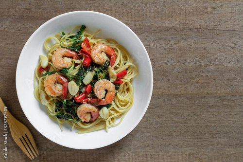 top view of stir fried spaghetti with shrimps and holy basil in a ceramic plate on wooden table. hot and spicy homemade style food menu.