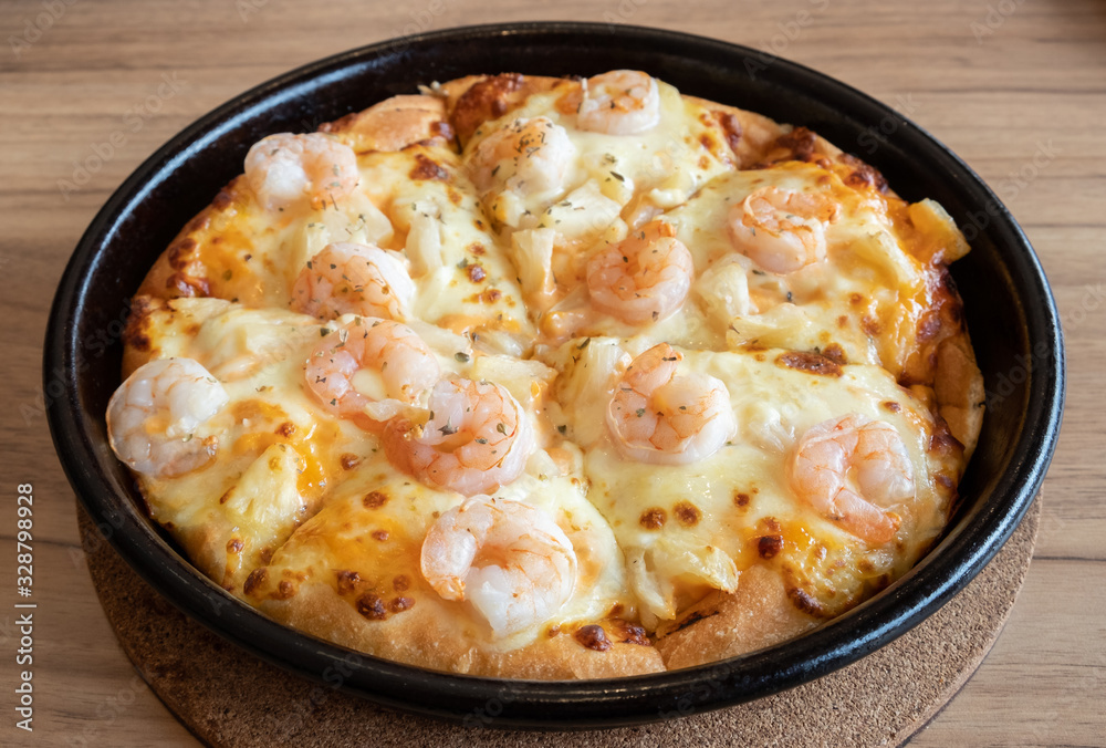 Close up of delicious seafood pizza topped with cheese, pineapple and shrimp on wooden table. Pizza is a favorite food for many around the world. Close up of delicious seafood pizza topped with cheese, pineapple and shrimp on wooden table. Pizza is a favorite food for many around the world.