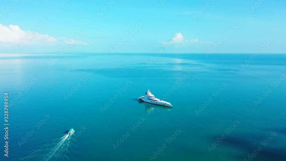 Beautiful big yacht anchoring on calm blue turquoise lagoon and boat sailing near shore of tropical island Beautiful big yacht anchoring on calm blue turquoise lagoon and boat sailing near shore of tropical island
